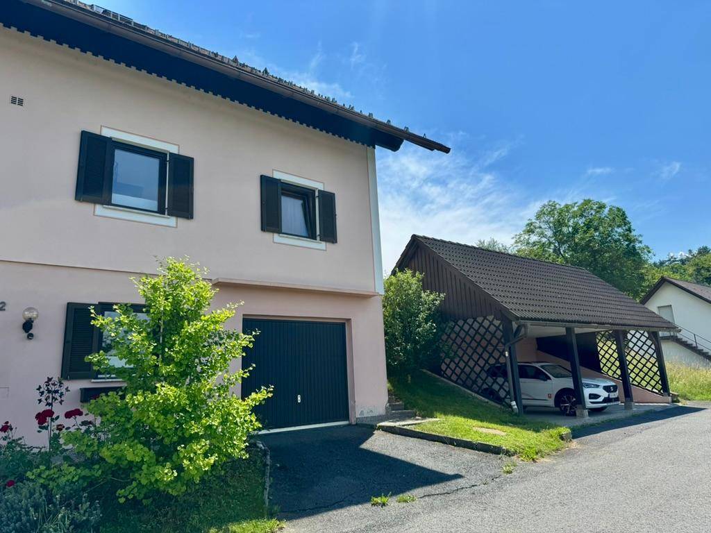 Seitenansicht des Hauses mit integrierter Garage und dem Carport, in dem ein Auto parkt.