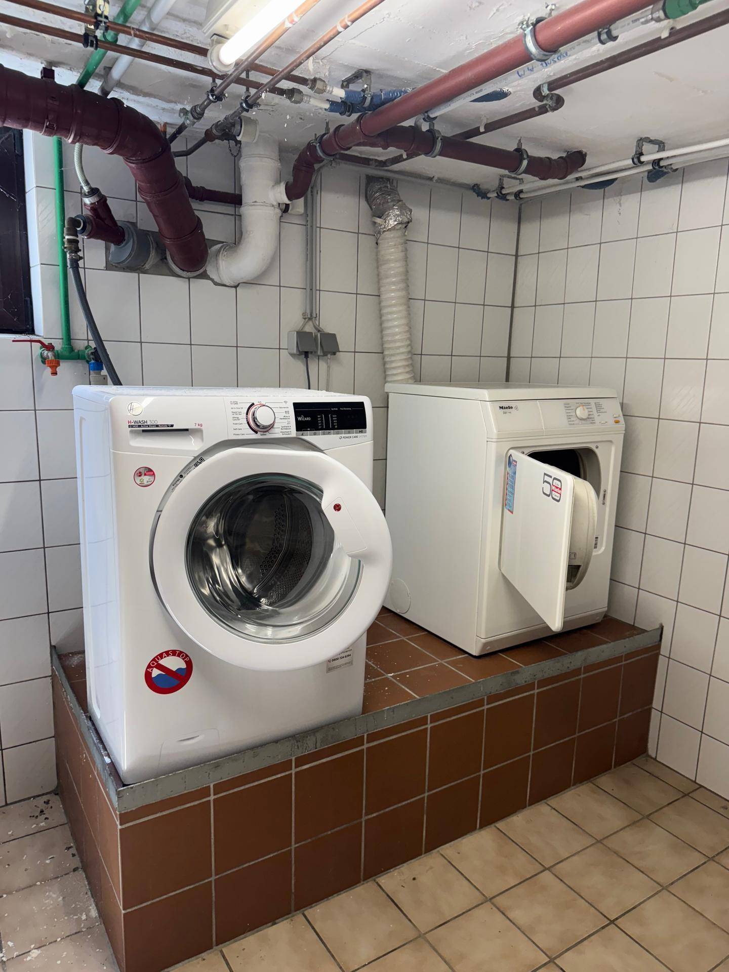 Waschküche mit Waschmaschine und Trockner, sowie sichtbaren Installationen an der Decke.