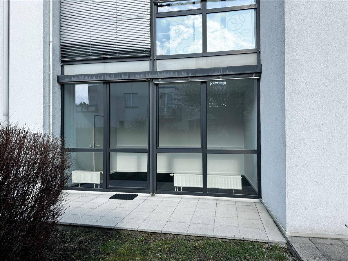 Erdgeschossfassade mit großen Glasfronten und einer kleinen gepflasterten Terrasse davor.