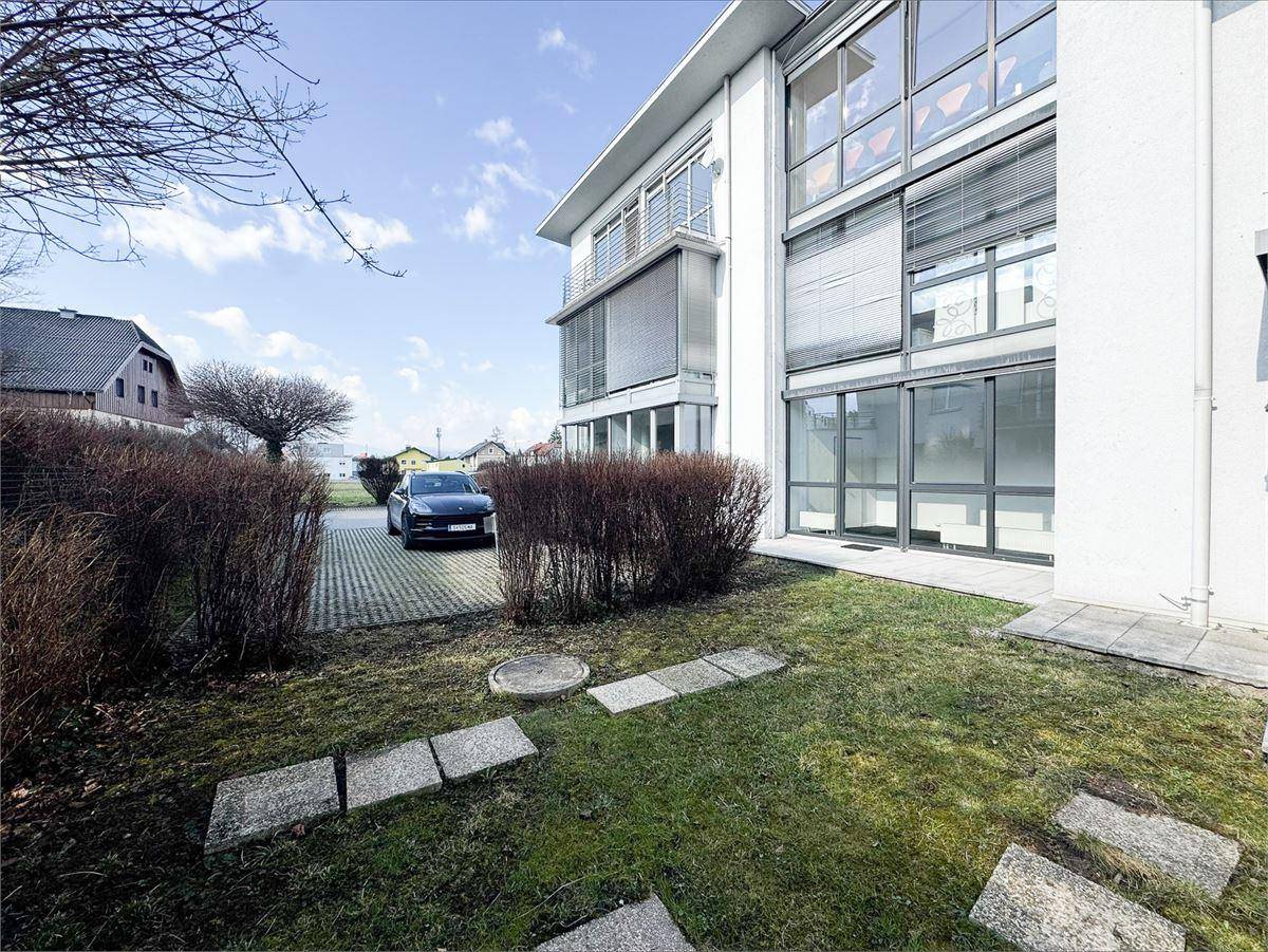 Außenansicht des Gebäudes mit Rasenfläche, Trittsteinen und einem gepflasterten Parkplatz.