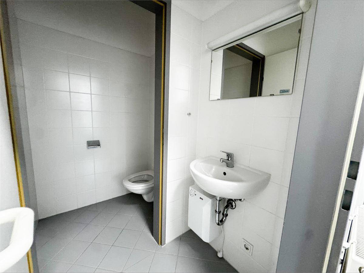 Einfache Toilette mit Waschbecken, Spiegel und hellgrauen Fliesen an Boden und Wänden.