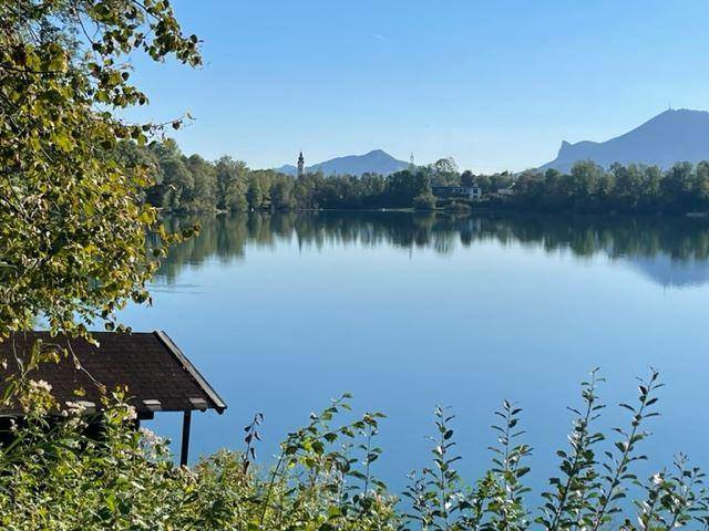 Idyllischer Seeblick mit Bergen im Hintergrund und einem kleinen Bootshaus am Ufer.