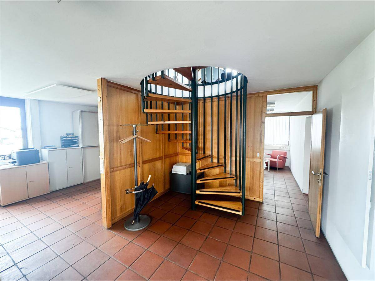 Bürofläche mit roter Akzentwand, großen Fenstern und durchgehenden Terrakottafliesen.