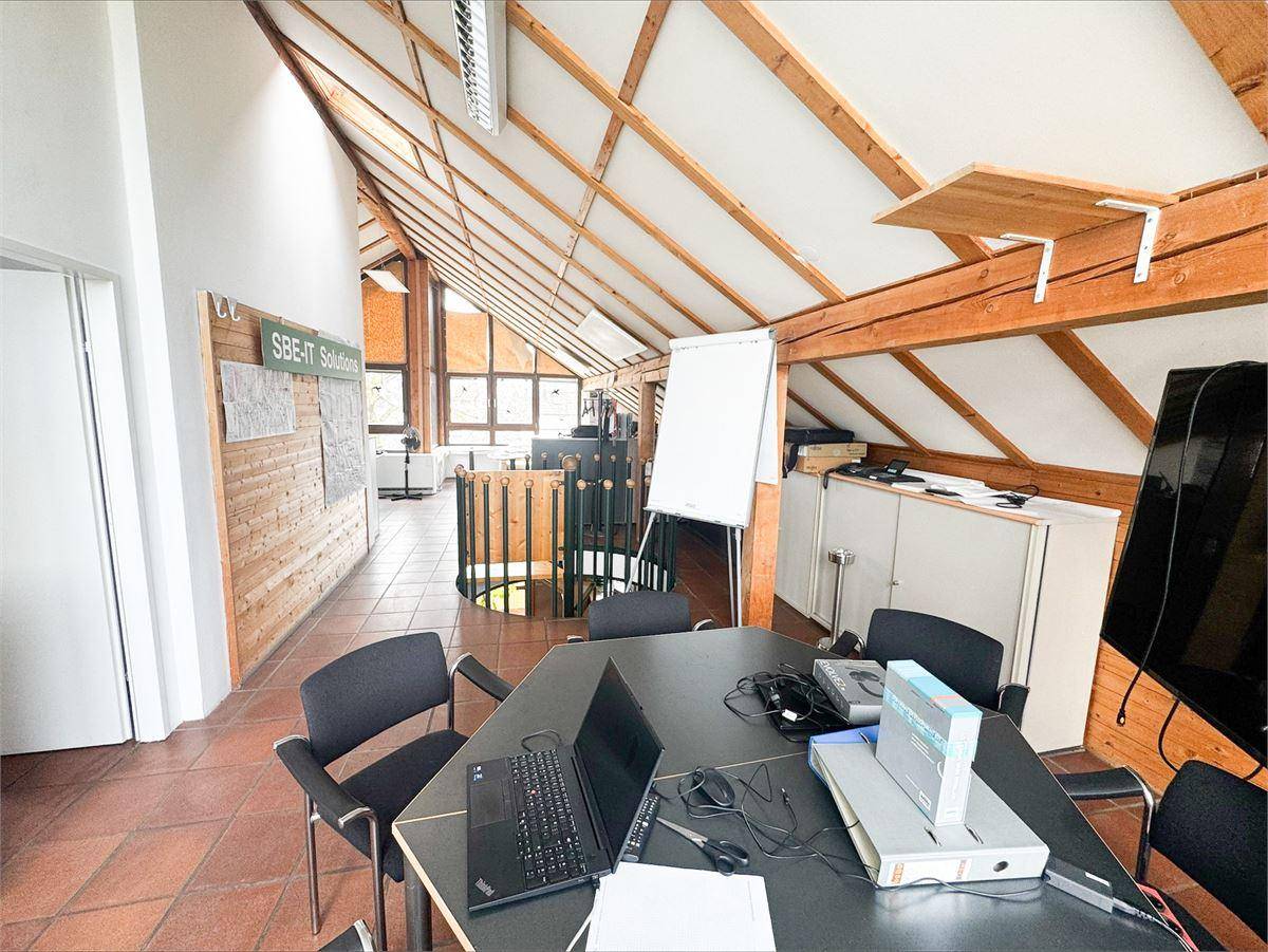 Empfangsbereich oder Bürofläche mit einer markanten Holz-Wendeltreppe und Terrakottafliesenboden.