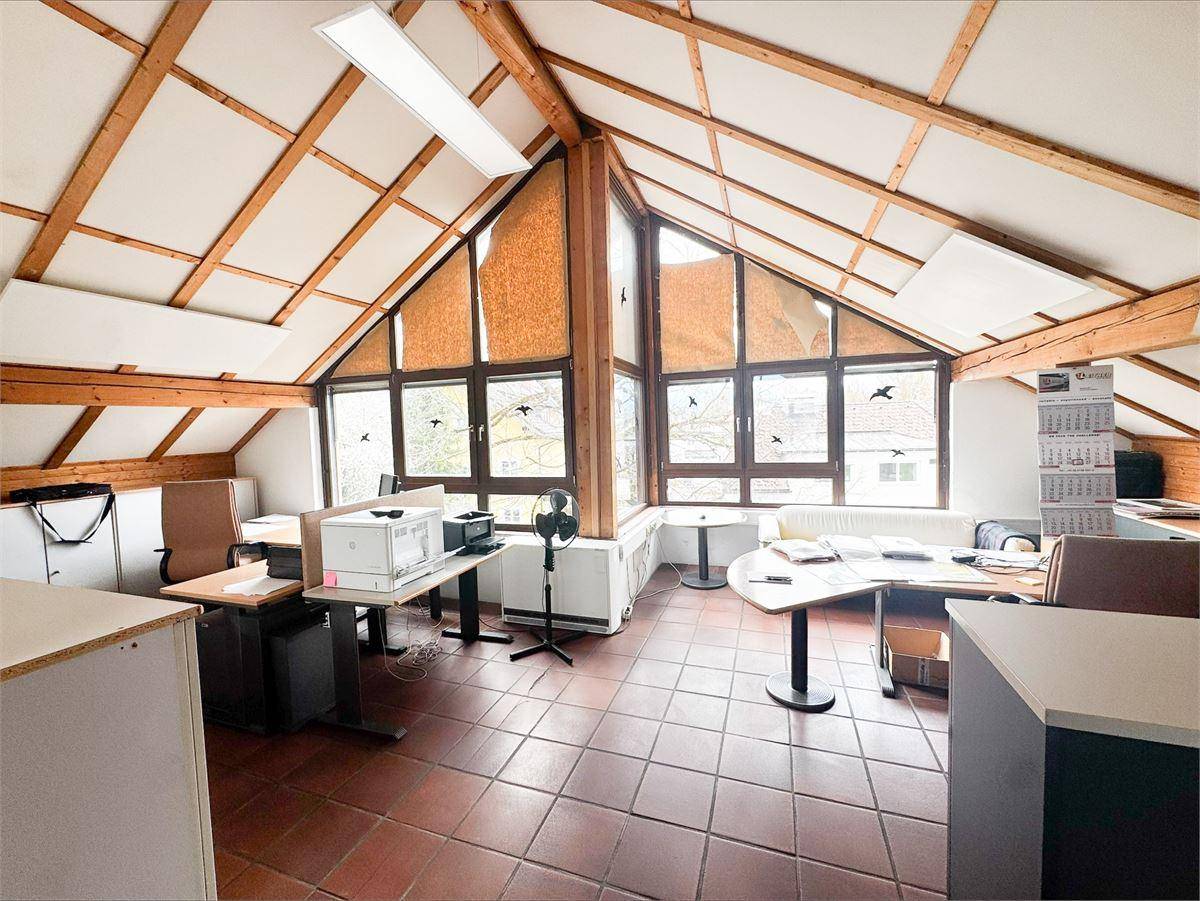 Heller Bürobereich im Dachgeschoss mit schrägen Decken, Holzbalken und funktionaler Einrichtung.