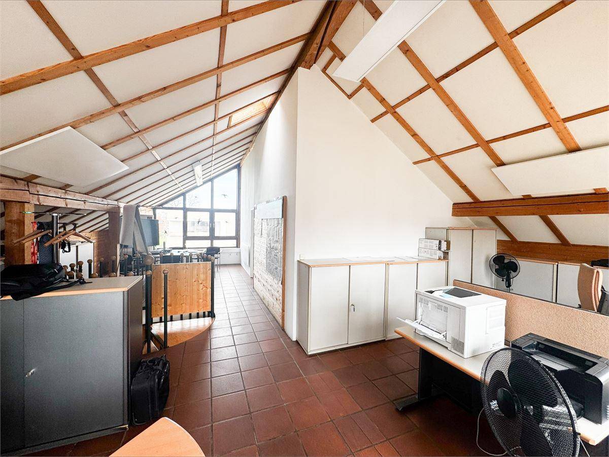 Konferenzbereich im Dachgeschoss mit Holzbalken, Terrakottafliesen und Blick auf eine Wendeltreppe.