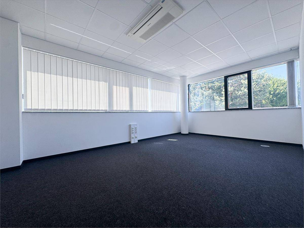 Helles Büro mit vertikalen Jalousien an den Fenstern und einem Klimagerät an der Decke.