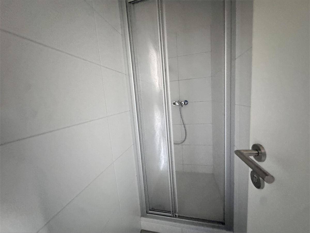 Einfache Duschkabine mit Falttür und weißen Fliesen in einem Badezimmer.