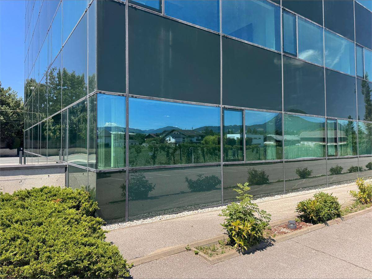 Modernes Bürogebäude mit großer Glasfassade, die die umliegende Landschaft und den blauen Himmel widerspiegelt.