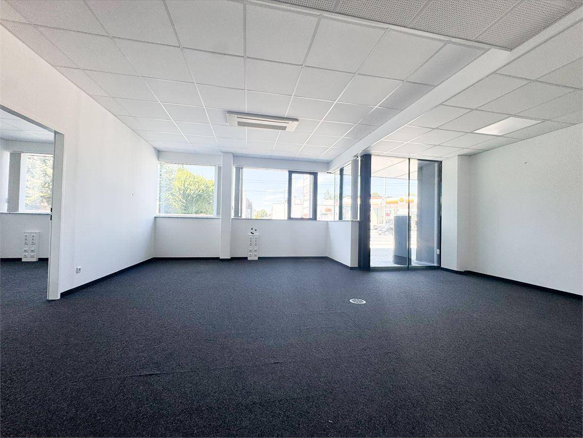 Geräumiger, leerer Büroraum mit großen Fenstern, viel Tageslicht und dunklem Teppichboden.