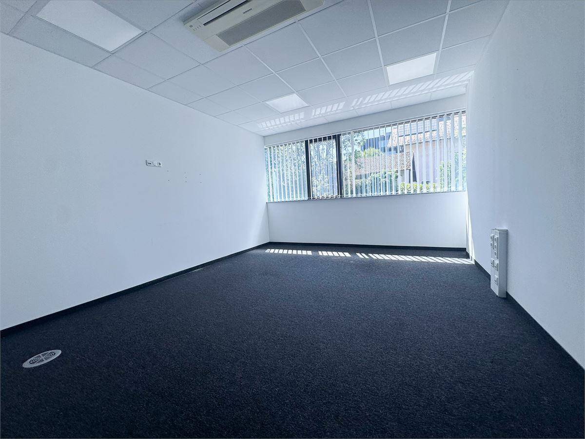 Heller Büroraum mit Jalousien an den Fenstern, dunklem Teppich und abgehängter Decke.