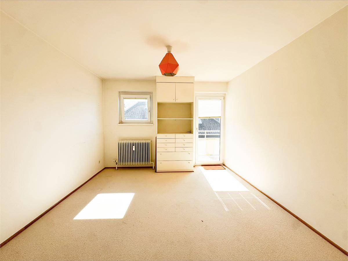 Sonniger Raum mit Teppichboden, Fenster und einem schmalen Schrank, vielseitig nutzbar.