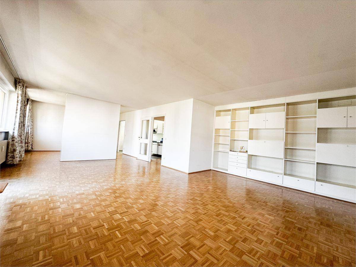 Geräumiges Wohnzimmer mit Fischgrätparkettboden und eingebauten weißen Regalen, bereit zur individuellen Gestaltung.