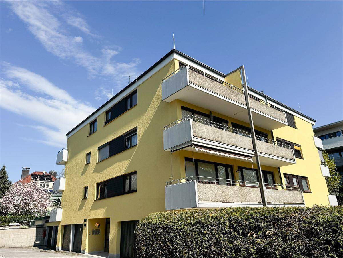 Gelbes Mehrfamilienhaus mit mehreren Balkonen und großen Fenstern unter blauem Himmel.