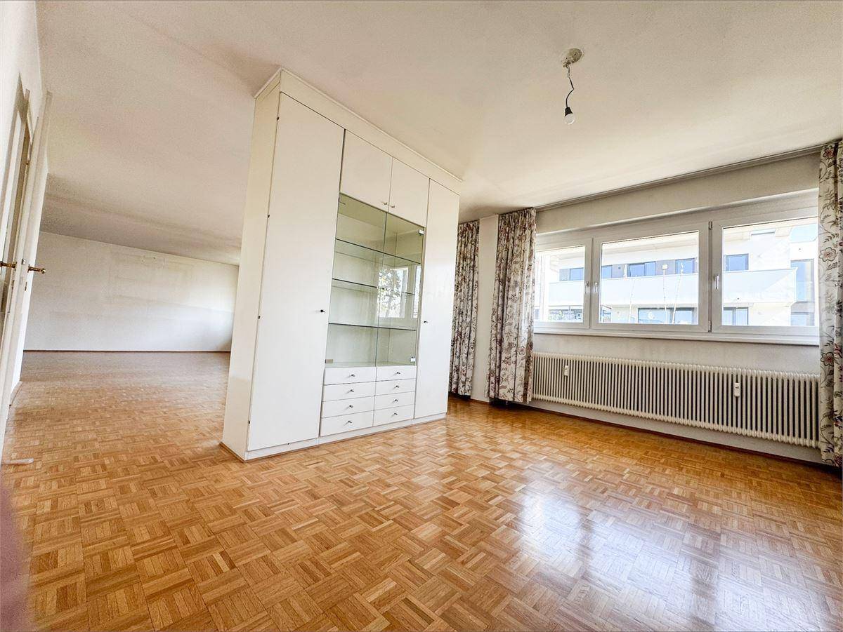 Helles Wohnzimmer mit Parkettboden, großem Fenster und einem integrierten Schrankelement.