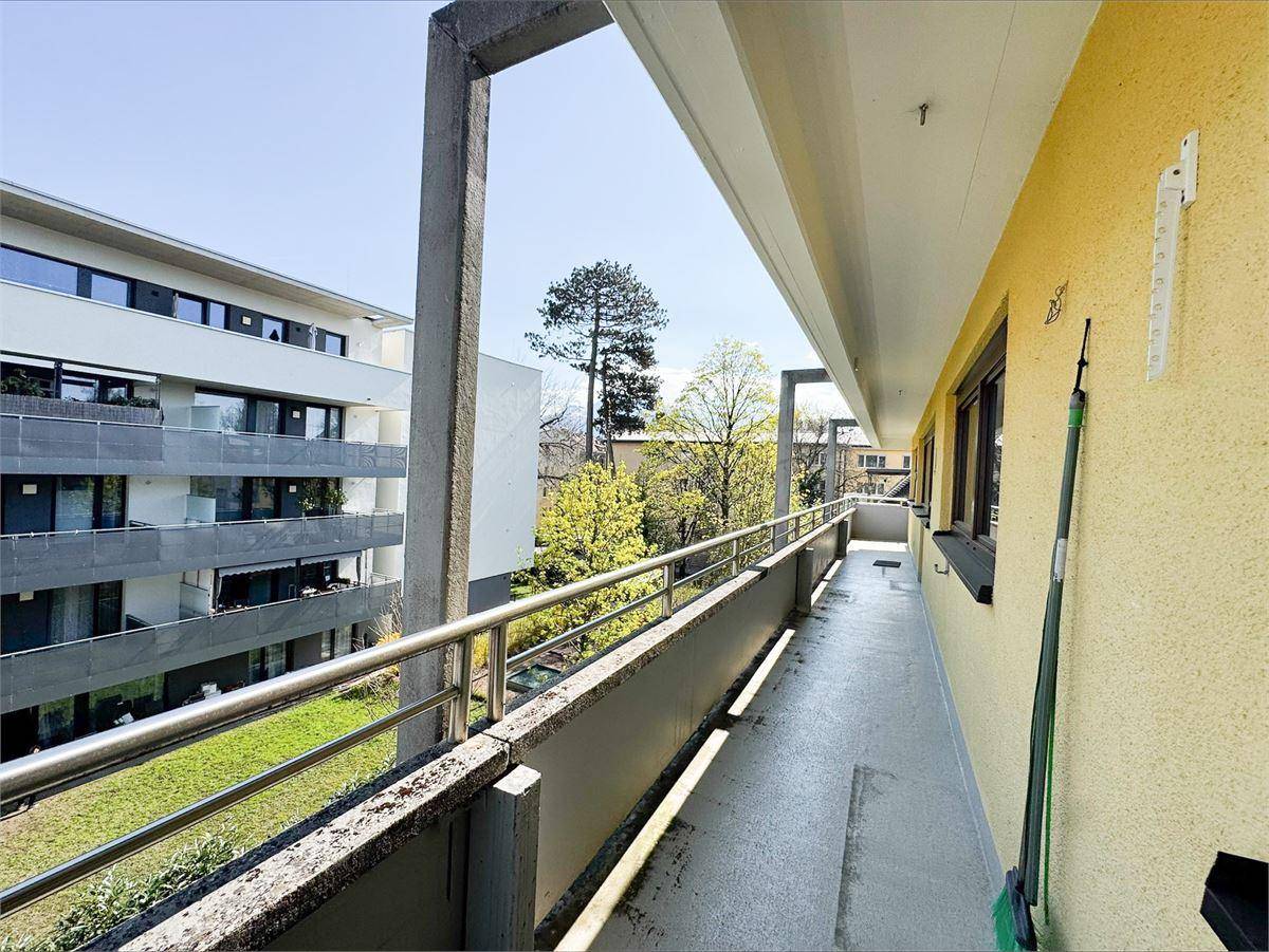 Langer Balkon mit Metallgeländer und Blick auf die benachbarten Gebäude und Grünflächen.