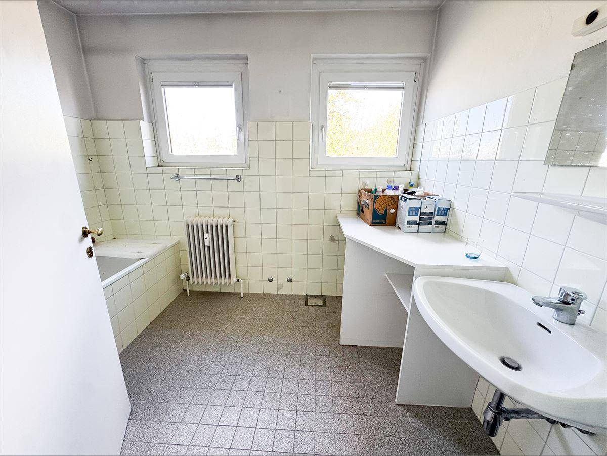 Badezimmer mit zwei Fenstern, Fliesen an den Wänden und einem Waschbecken mit Ablagefläche.