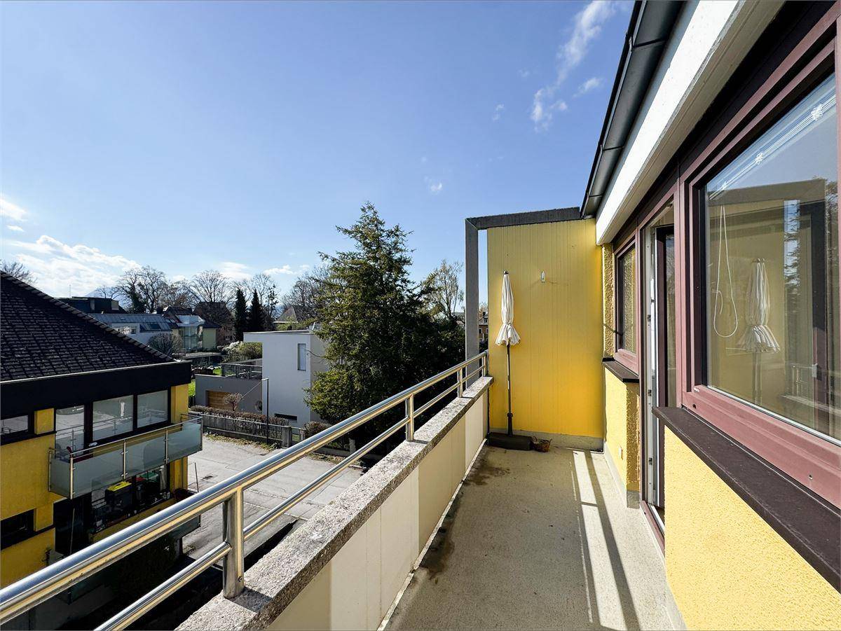 Heller Balkon mit Metallgeländer und Blick auf die umliegende Wohngegend unter blauem Himmel.