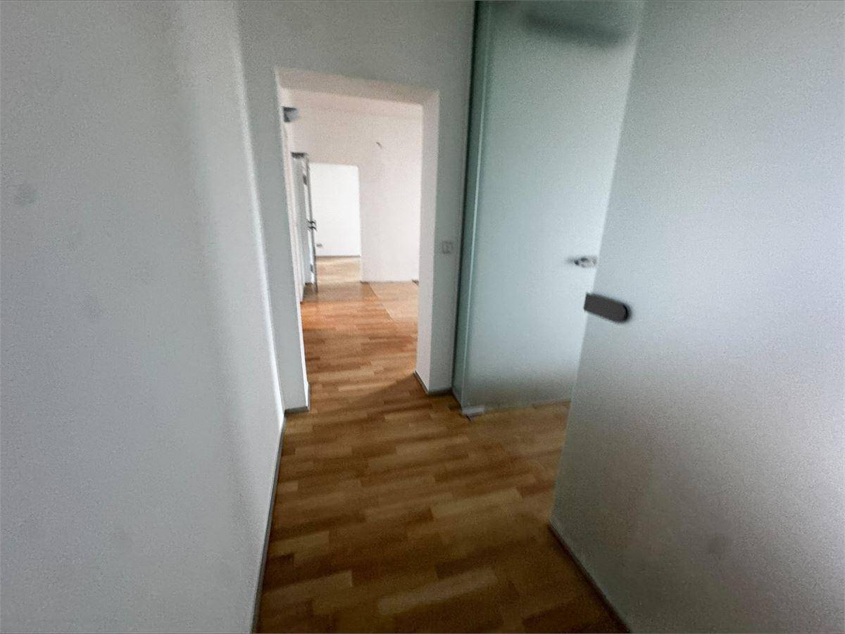 Langer Flur mit hellem Parkettboden, weißen Wänden und einer Milchglastür, die zu weiteren Räumen führt.