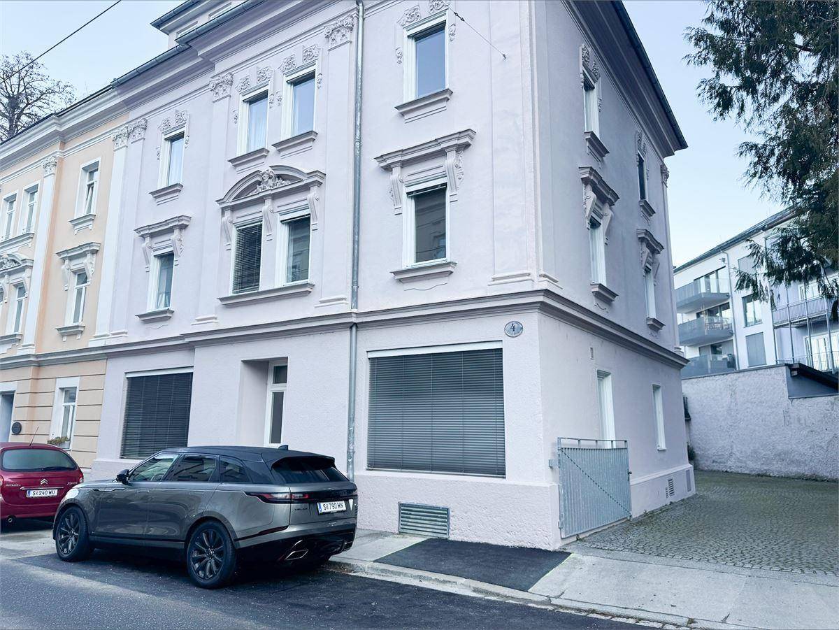 Eckansicht des historischen Gebäudes mit aufwendiger Fassade, großen Fenstern und geparkten Autos davor.