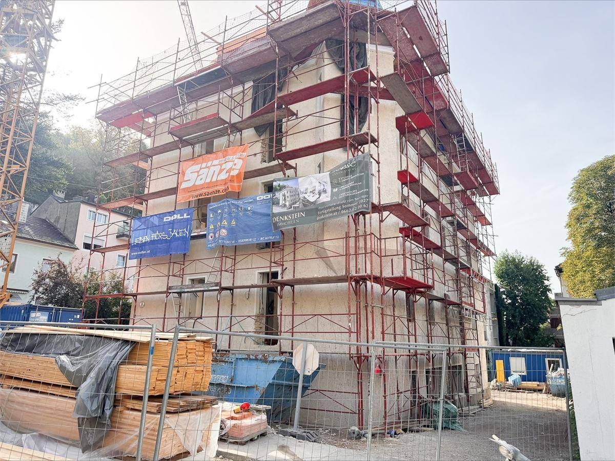 Gebäude unter Gerüst für Renovierungsarbeiten mit Baumaterialien und Kran auf der Baustelle.