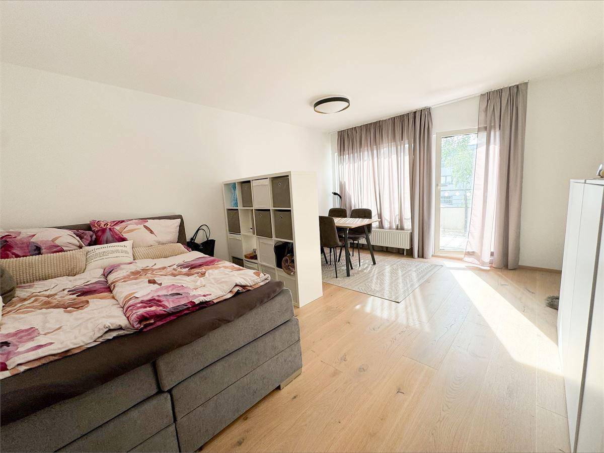 Kombinierter Wohn- und Schlafbereich mit Holzboden, Esstisch und Zugang zum Balkon.