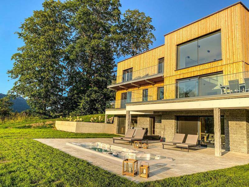 Moderne Architektur mit Holzfassade, großen Glasflächen und einer weitläufigen Terrasse mit Pool und Liegewiese.