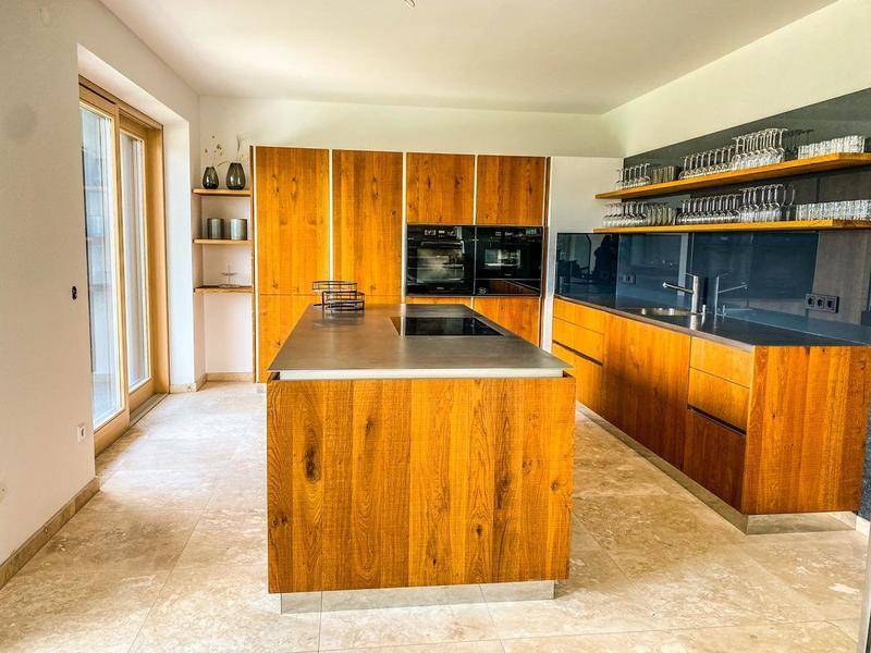 Moderne Holzküche mit Kochinsel, integrierten Geräten und Zugang zur Terrasse.