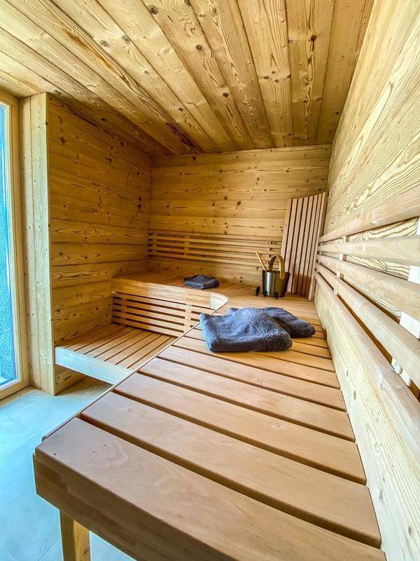 Geräumige Holzsauna mit mehreren Bänken und natürlichem Lichteinfall durch ein kleines Fenster.