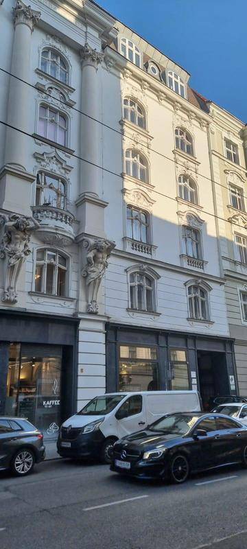 Historisches Gebäude mit klassischer Architektur, verzierten Fenstern und Geschäften im Erdgeschoss an einer Straße.