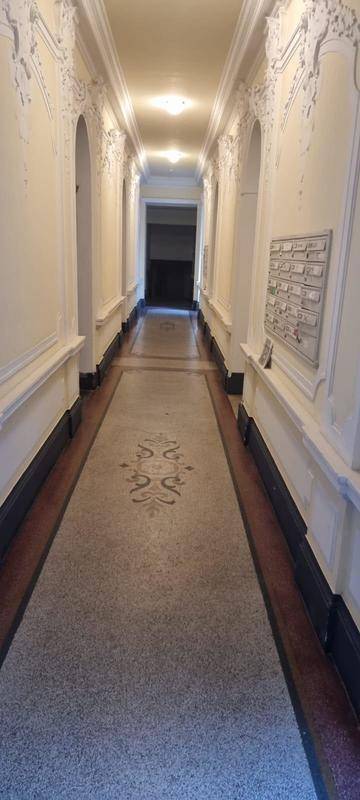 Langer, eleganter Flur mit gemustertem Terrazzoboden und verzierten Wänden in einem historischen Gebäude.