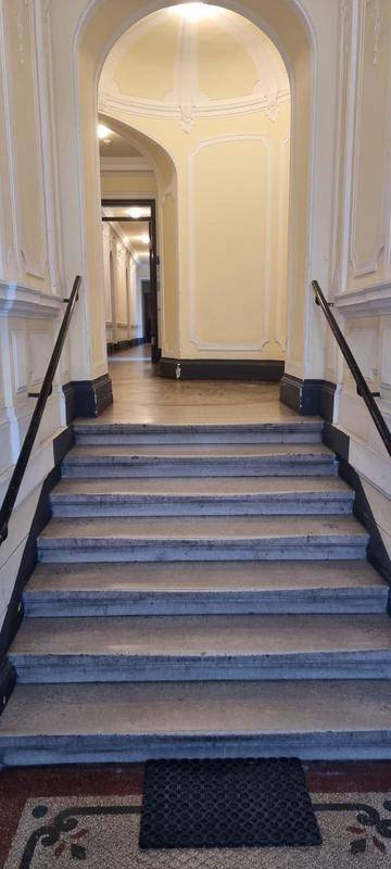 Breite Steintreppe mit Geländer in einem eleganten Eingangsbereich mit Rundbögen und hohen Decken.