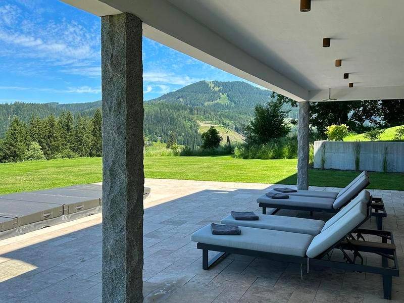 Überdachte Terrasse mit bequemen Liegestühlen und weitem Blick auf die grüne Berglandschaft.