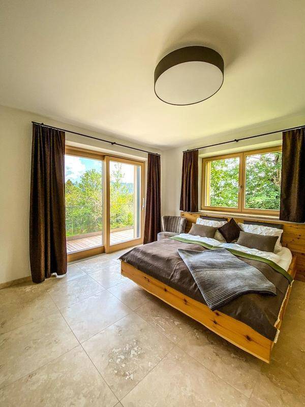 Helles Schlafzimmer mit Holzbett, großen Fenstern und Zugang zu einem Balkon, mit Blick ins Grüne.