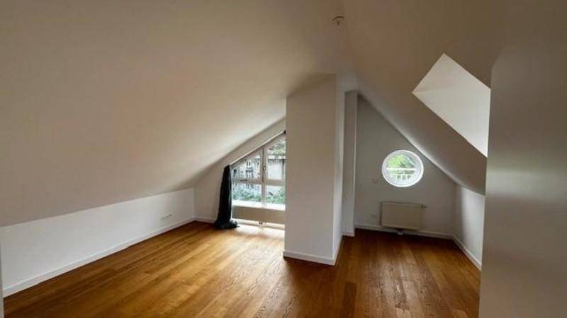 Gemütliches Dachzimmer mit Holzboden, schrägen Decken und einem charmanten Rundfenster.