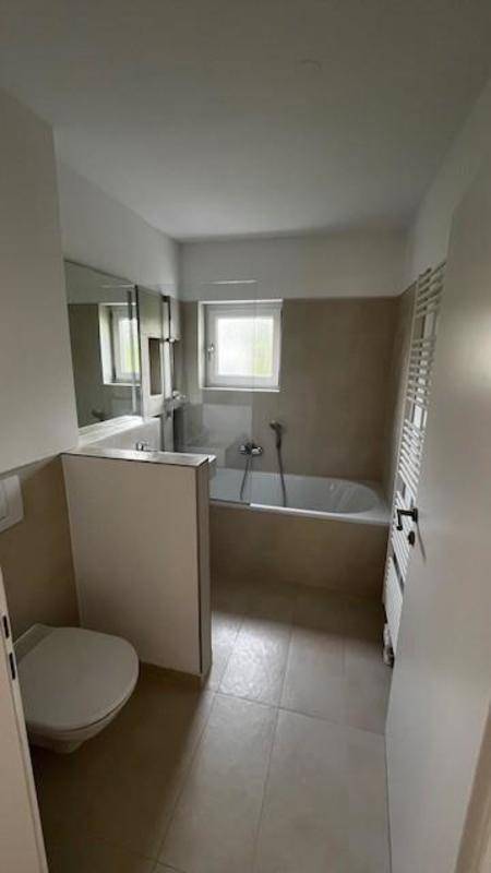 Modernes Badezimmer mit Badewanne, WC, Fenster und beheiztem Handtuchhalter.