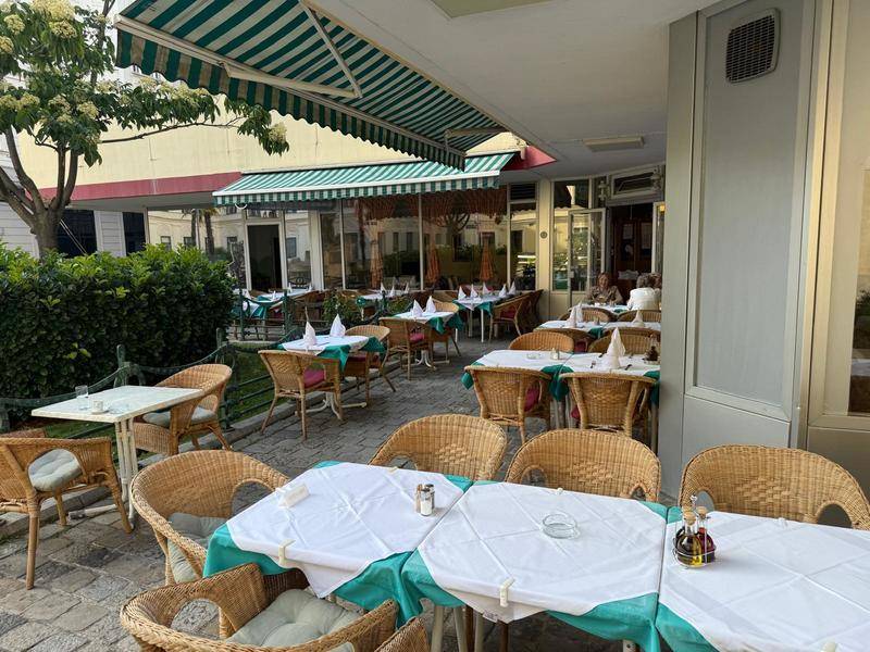 Eine weitläufige Außenterrasse eines Restaurants mit mehreren Tischen und gestreiften Markisen.