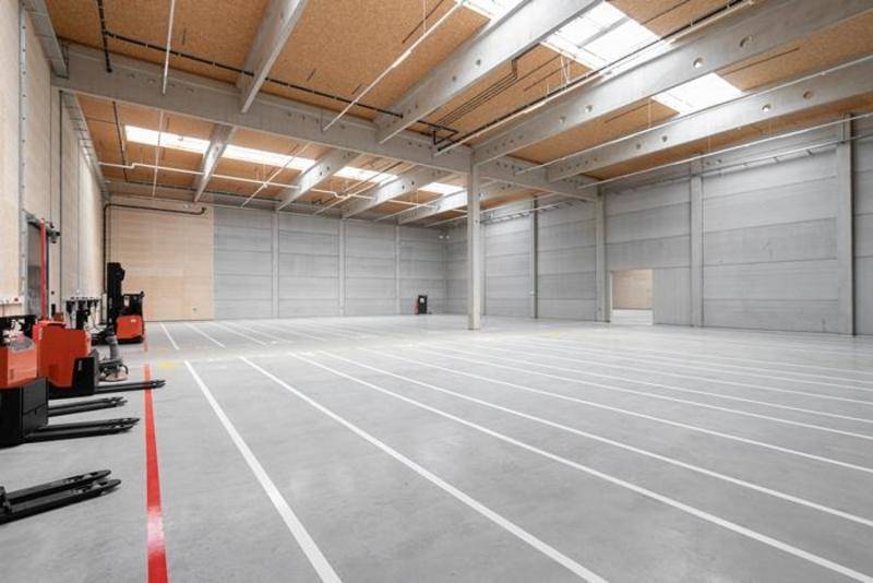 Sehr große, leere Lagerhalle mit hohen Decken, Oberlichtern und sauberem Betonboden, bereit zur Nutzung.