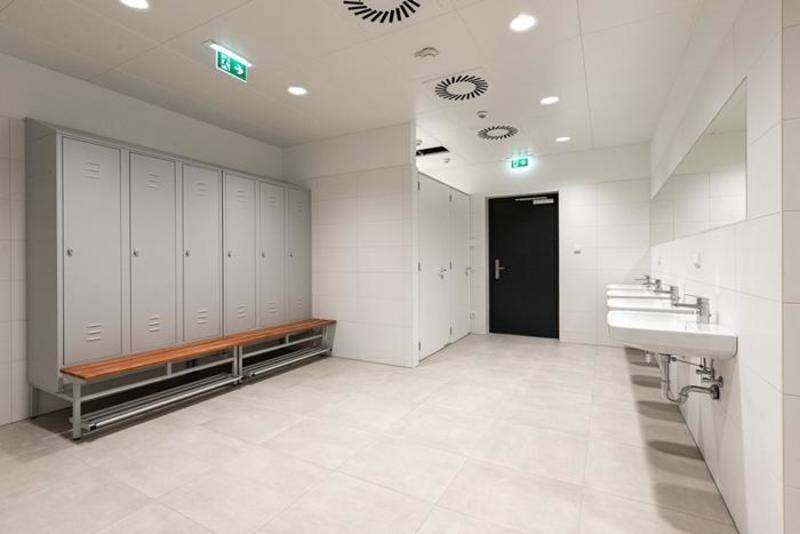 Geräumiger Umkleideraum mit Reihen von Spinden, Waschbecken und einer Sitzbank in heller, sauberer Umgebung.