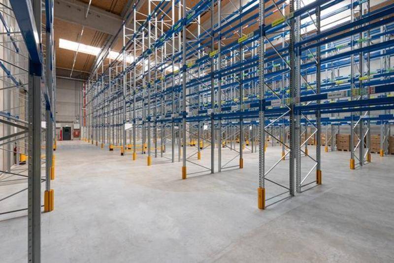 Weitläufige Lagerhalle mit hohen Regalsystemen und Betonboden, bereit für die Einlagerung von Waren.