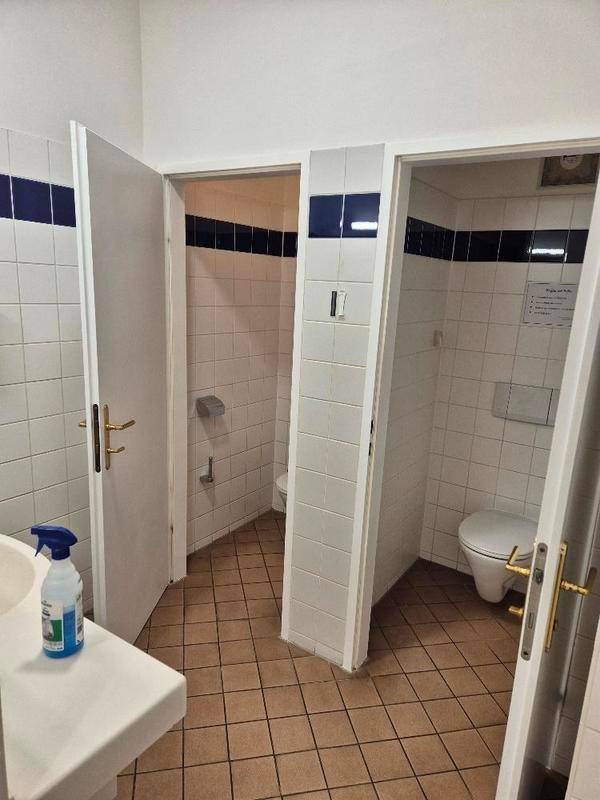 Gefliester Gemeinschafts-Waschraum mit mehreren Toilettenkabinen und einem Waschbecken.