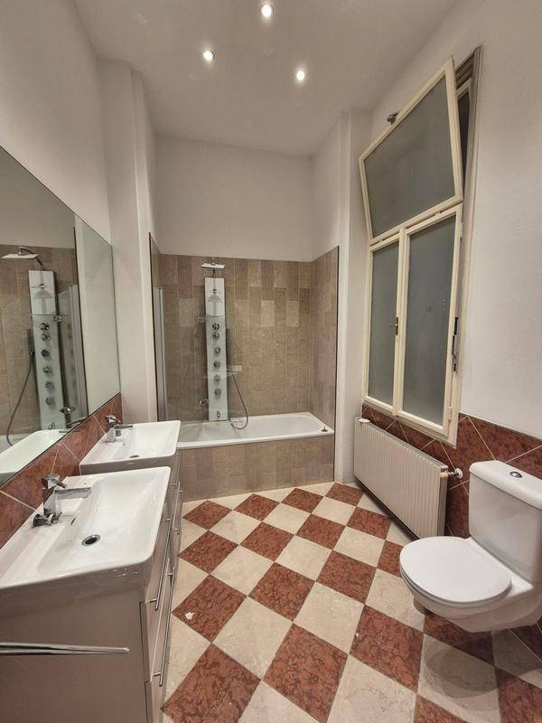 Modernes Badezimmer mit rot-weiß kariertem Fliesenboden, Doppelwaschbecken, Badewanne und Fenster.