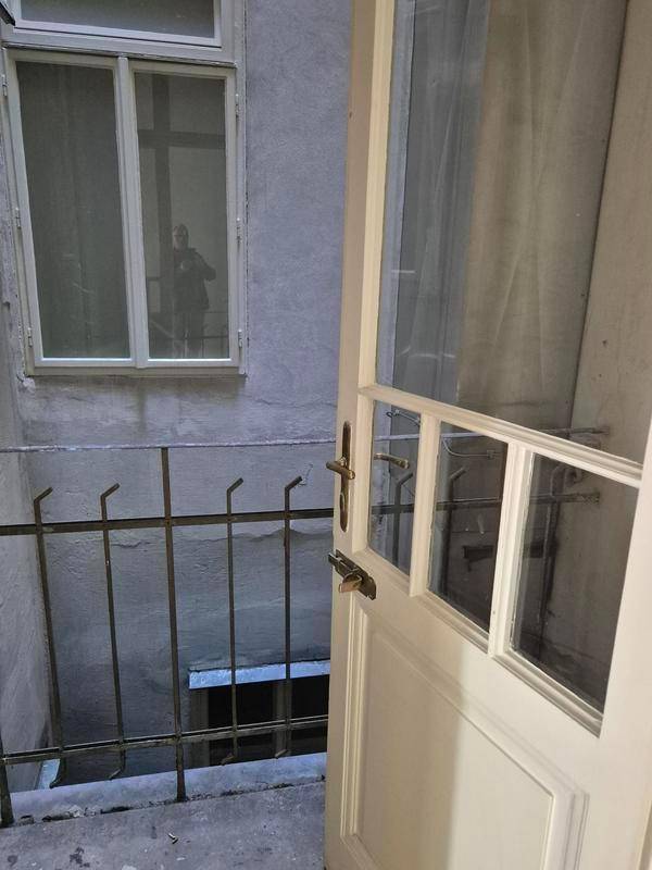 Blick durch eine offene Tür in einen kleinen, einfachen Innenhof mit Gitter und einem Fenster.