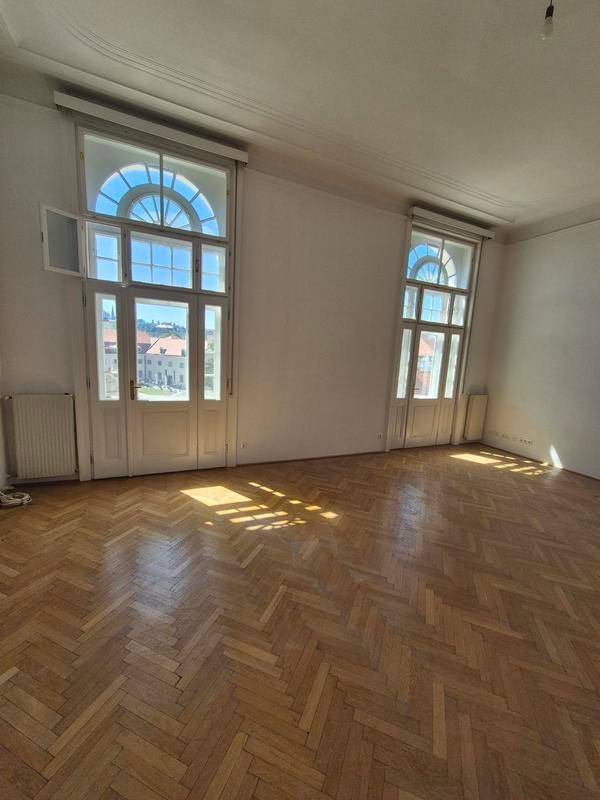 Helles Wohnzimmer mit klassischem Fischgrätparkett und hohen Fenstertüren, die den Raum mit Sonnenlicht füllen.
