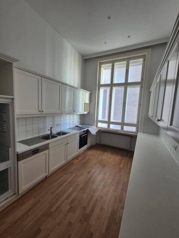 Helle Küche mit weißen Einbauschränken, Holzboden und einem großen Fenster, das viel Tageslicht spendet.