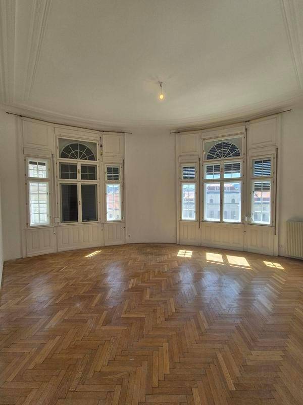Geräumiges Wohnzimmer mit Fischgrätparkett und zwei großen, eleganten Bogenfenstern, die viel Licht hereinlassen.