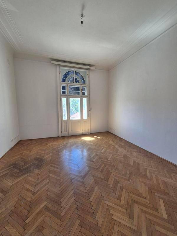 Geräumiges Zimmer mit klassischem Fischgrätparkett und einer hohen Fenstertür, die den Raum erhellt.
