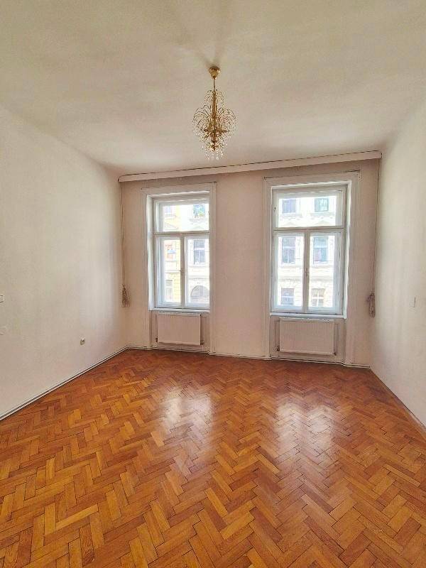 Helles Zimmer mit klassischem Fischgrätparkett, hohen Decken und elegantem Kronleuchter.