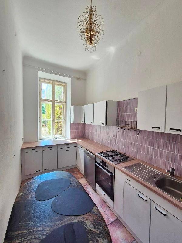 Küche mit weißen Schränken, rosa Fliesenrückwand, Gasherd und Blick ins Grüne.