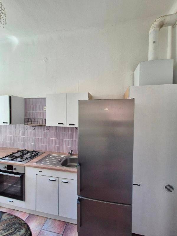Küche mit weißen Schränken, Gasherd, Backofen und einem modernen Edelstahlkühlschrank.